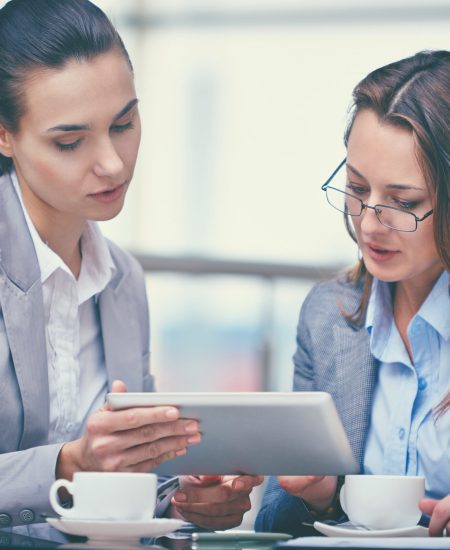 Image of two confident businesswomen working with touchpad in office